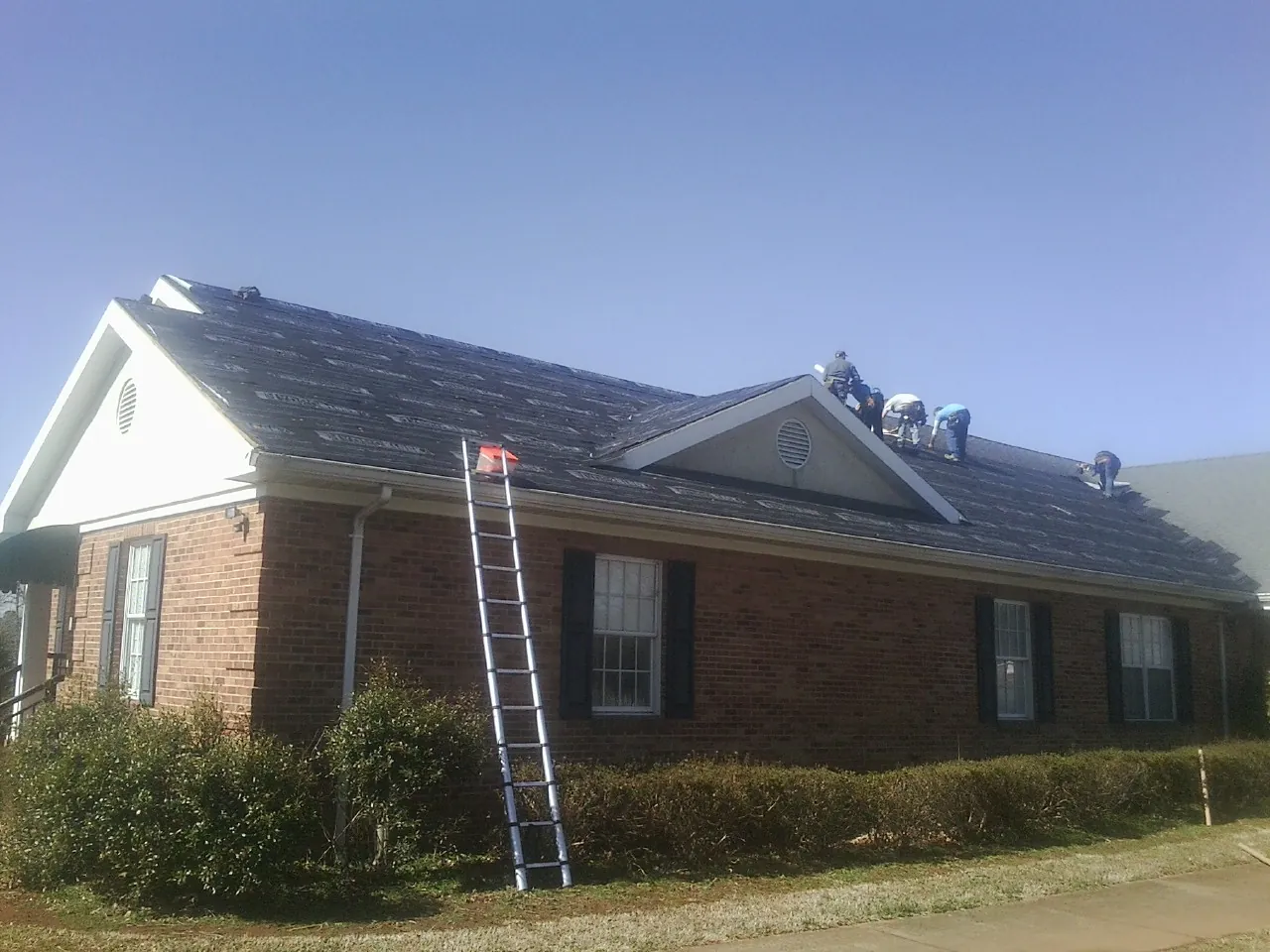 Crew tearing shingles off a brick ranch roof with a ladder set — Metal Roof Repair work by our crew in Bannock