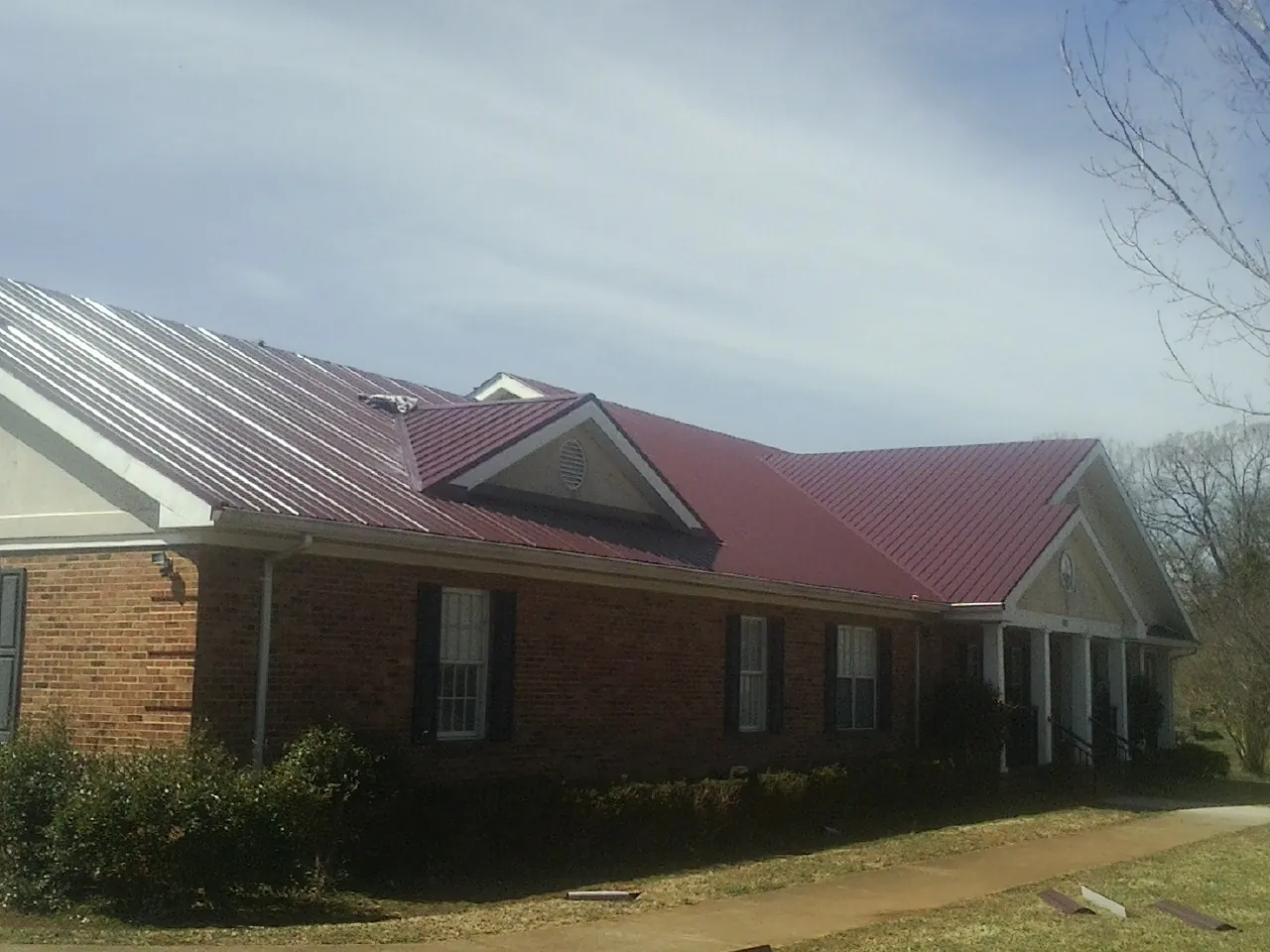 Red metal roof with gabled entries on a long brick building, from a Hail Damage Roof Repair job in Bannock
