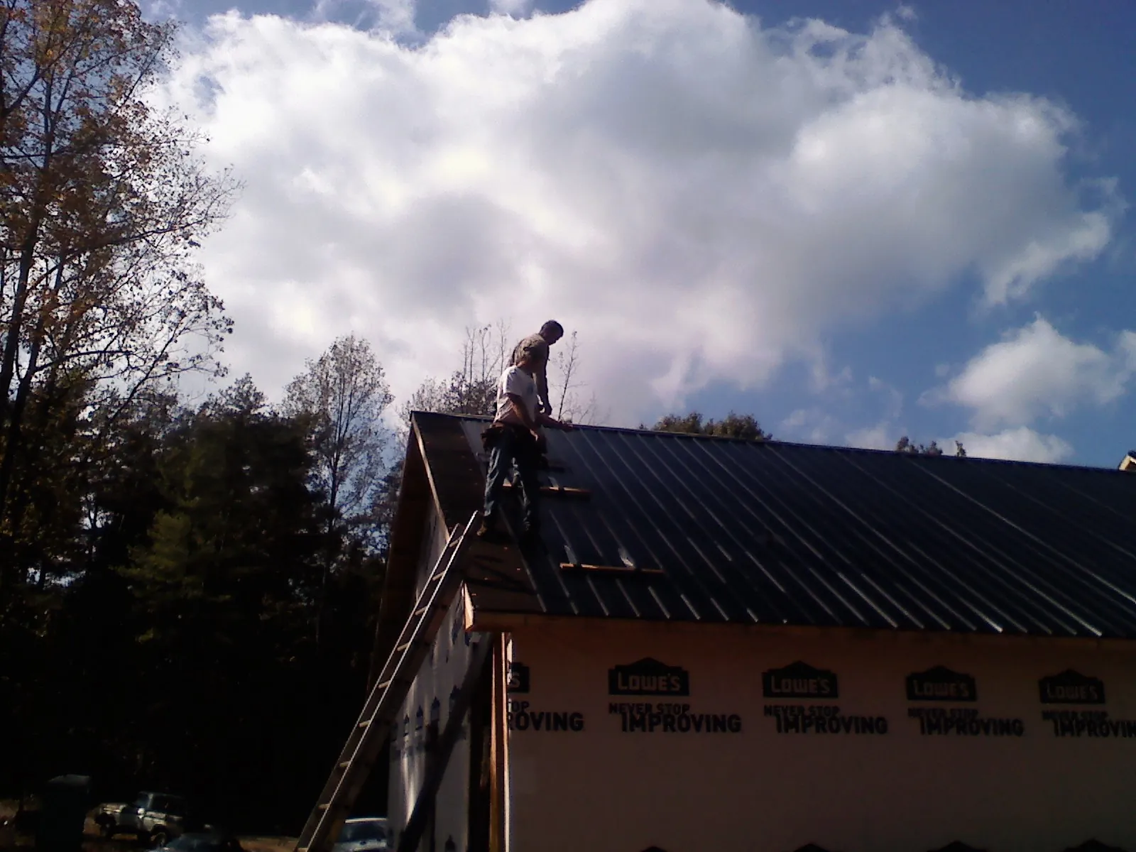 Roofer fastening dark metal panels high against a cloudy sky, from a Roof Inspection job in Bannock