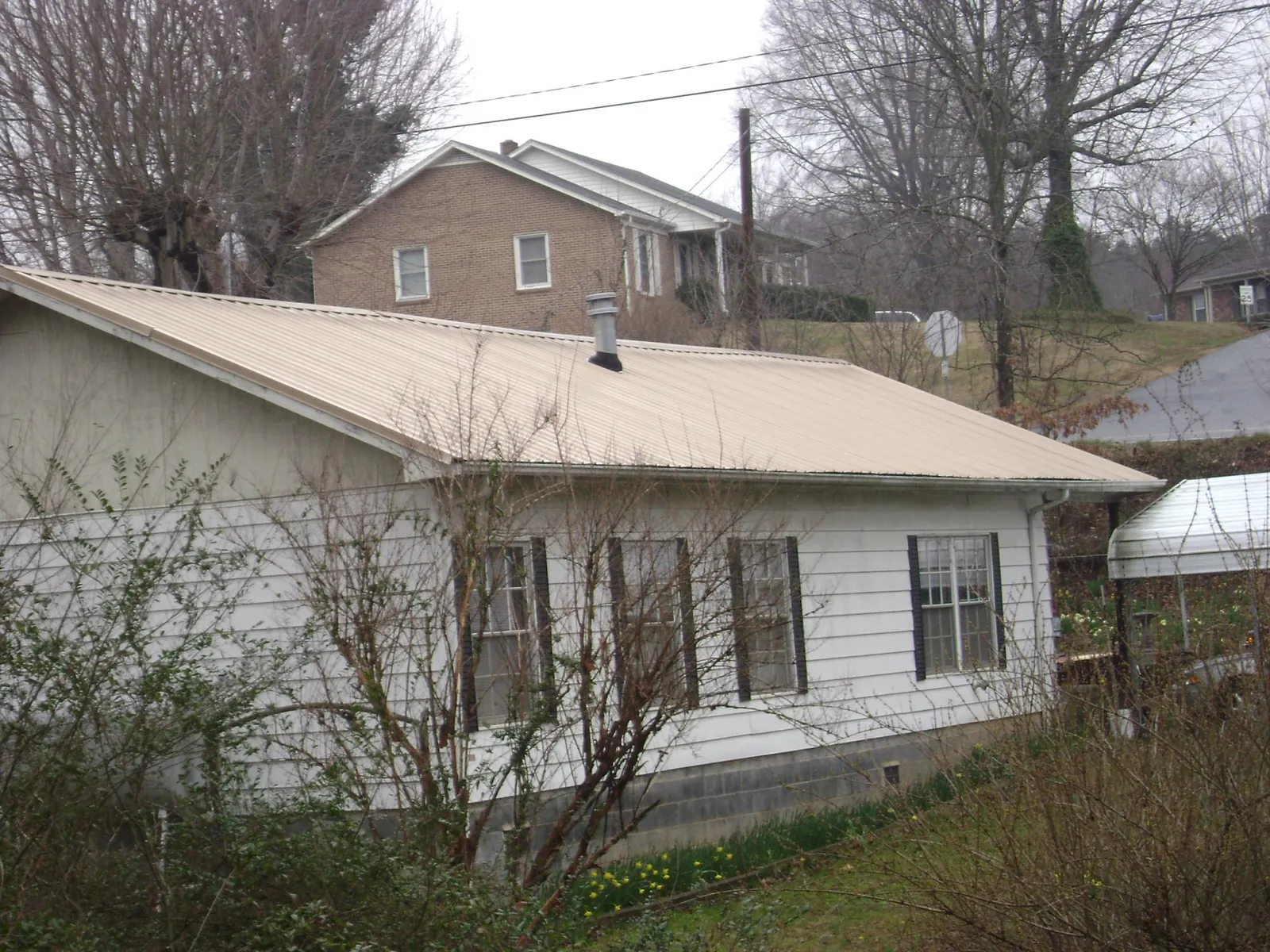 Tan metal roof on a white sided house set into a hillside — Commercial Roofing by Roofing Brothers in Bannock